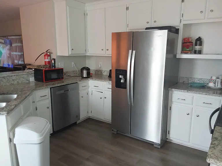 Kitchen features granite-look counters, ample white cabinetry, and stainless steel appliances including a side-by-side fridge