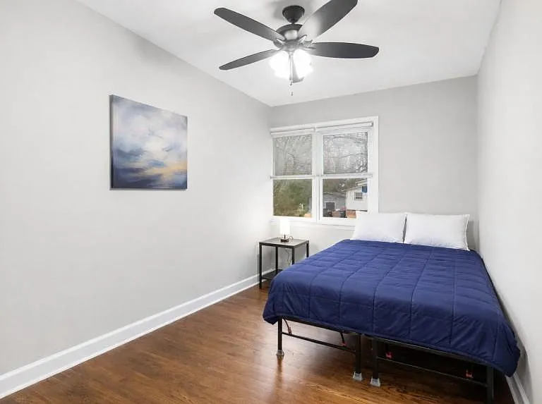 Private bedroom features a ceiling fan, hardwood-style floors, and a window for natural light, plus space for a nightstand.