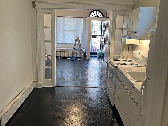 View of kitchen thru to living room with large front window, beautiful vestibule with ornate hardwood trim with glass door and beautiful trim with glass pane entrance just refinished floors and walls.