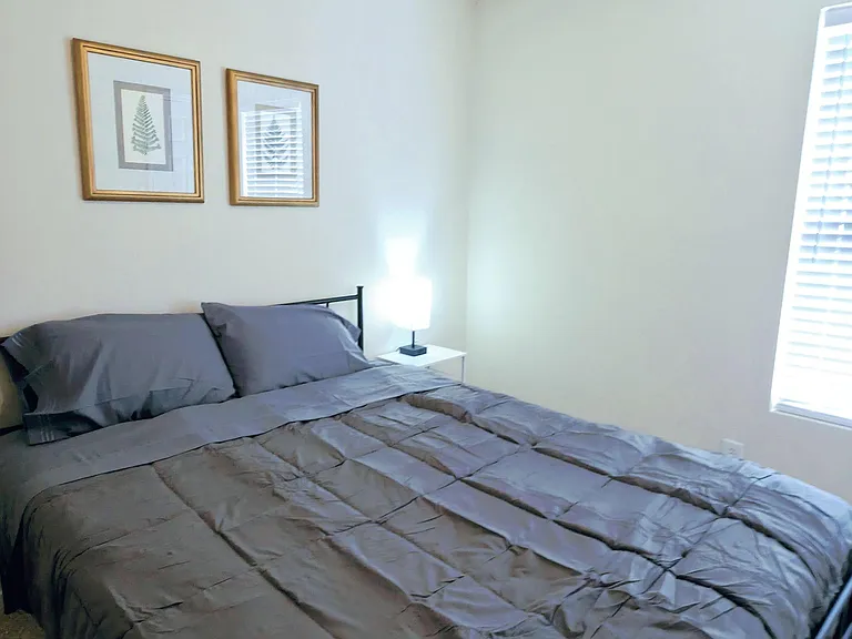 Furnished bedroom with a full-size bed, nightstand lighting, and ceiling fan, plus a window with blinds for privacy.