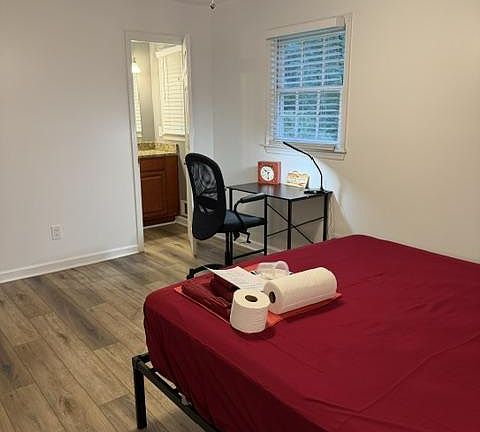 Private bedroom with wood-style flooring, ceiling fan, and a workspace by the window, plus convenient access to a nearby bath