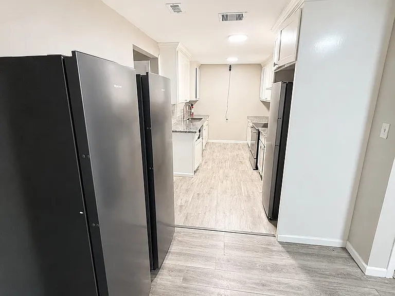Galley kitchen with ample cabinet storage, granite-look counters, and black appliances, plus durable wood-style flooring.