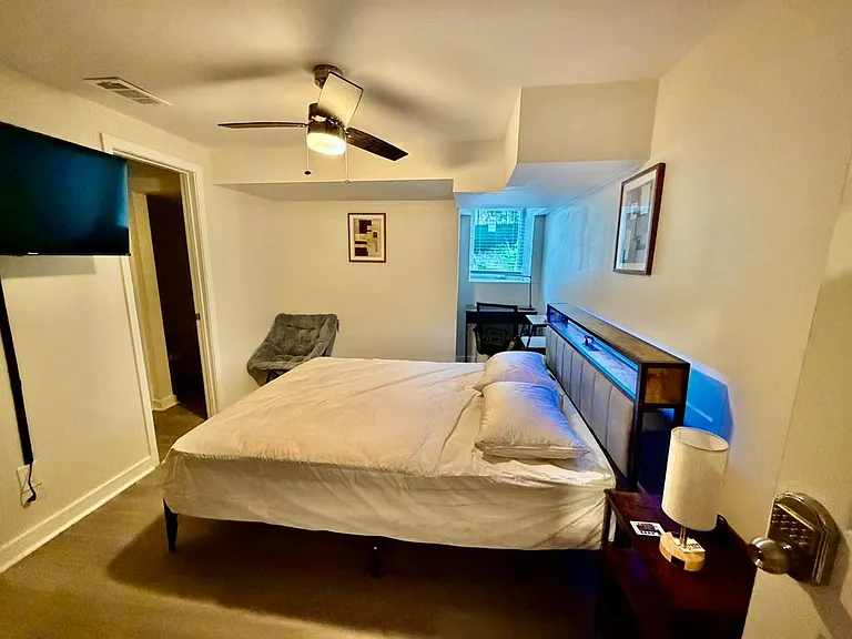 Furnished bedroom with a ceiling fan, wall-mounted TV, and a work desk by the window for studying or remote work.