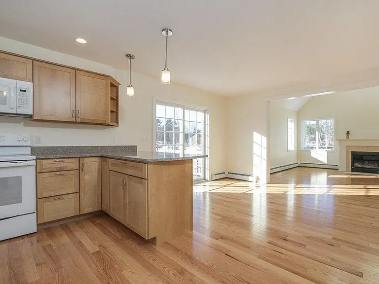 View of light-filled 1st floor living area from inside front entry. Kitchen through dining area with deck, living room with gas fireplace. NOTE white appliances were replaced with stainless steel