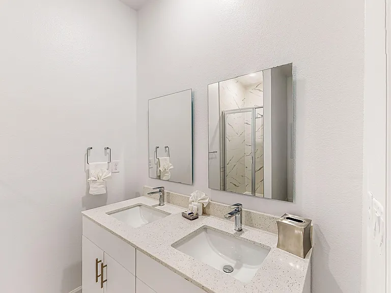 Clean bathroom vanity with dual sinks, sleek fixtures, and oversized mirrors; glass-enclosed shower with tile surround.