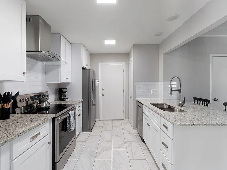 Kitchen featuring appliances with stainless steel finishes, wall chimney exhaust hood, light marble finish flooring, white cabinets, and light stone countertops