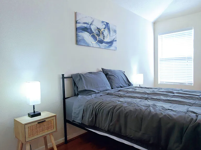 Private bedroom with a full bed, nightstand lighting, and a window with blinds over easy-care wood-look floors.
