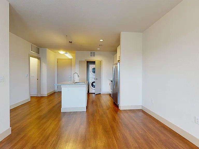 Apartment kitchen with stainless steel appliances, dining and living room with wood-style flooring.