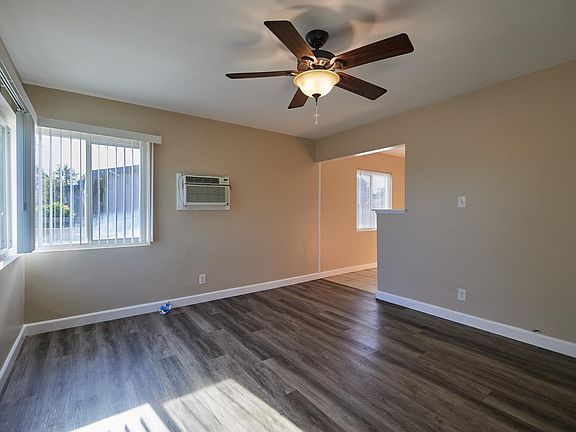 Entrance into the living room, complete with wood laminate flooring, fresh paint, big windows to bring in natural light, ceiling fan, and wall air.