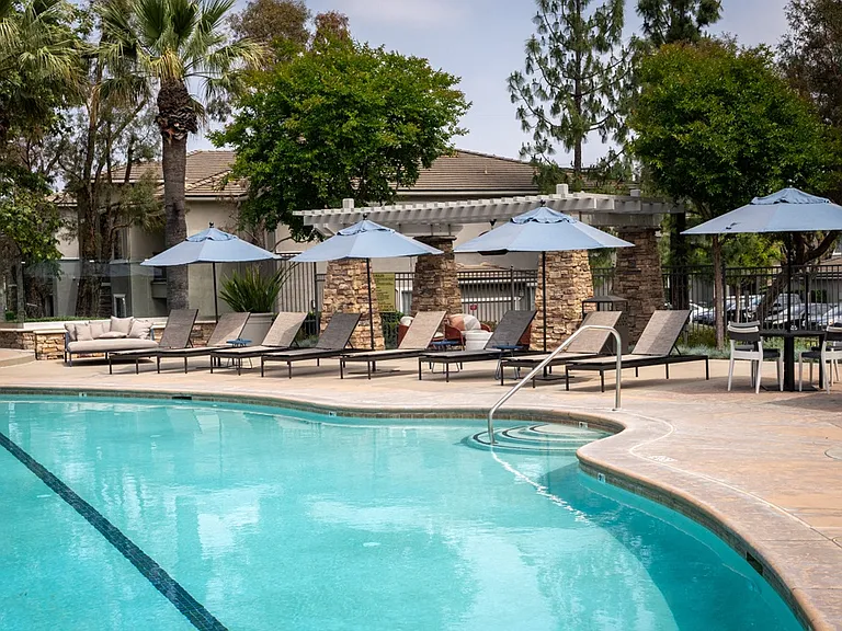 Resort-Style Pool Area with Umbrella-Covered Loungers and Stone Pergola