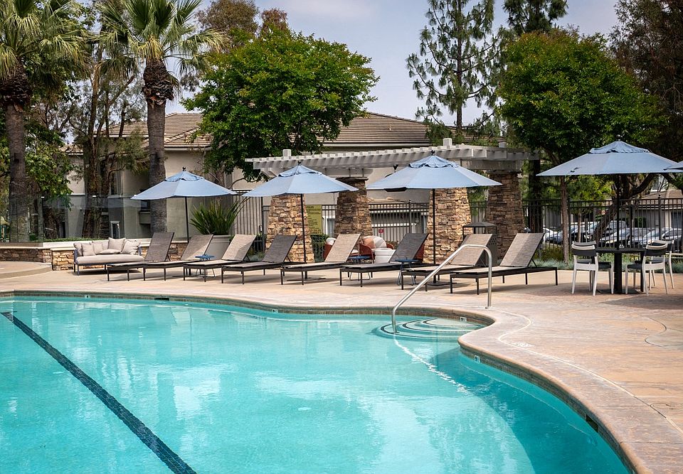 Resort-Style Pool Area with Umbrella-Covered Loungers and Stone Pergola