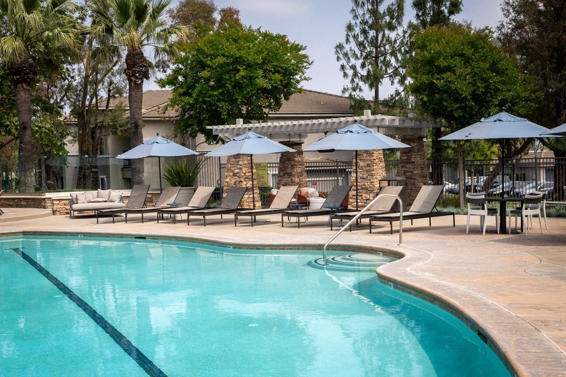 Resort-Style Pool Area with Umbrella-Covered Loungers and Stone Pergola