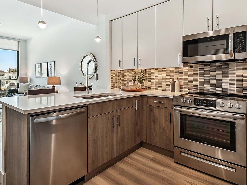 Griffis West Palm apartment kitchen with wood style floor and cabinets, tiled backsplash, and stainless steel appliances.