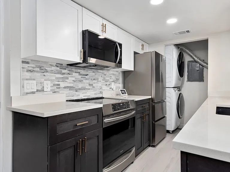 Kitchen with backsplash, stacked washer / drying machine, white cabinetry, and stainless steel appliances