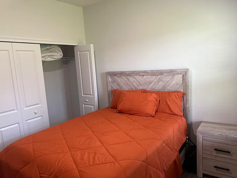 Furnished bedroom with a comfortable bed, nightstand, and a closet with shelving for convenient everyday storage.