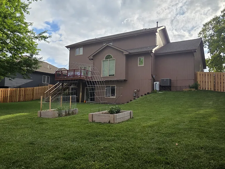 Backyard featuring large lawn, deck with sliding door to kitchen, walkout basement, and raised garden beds.