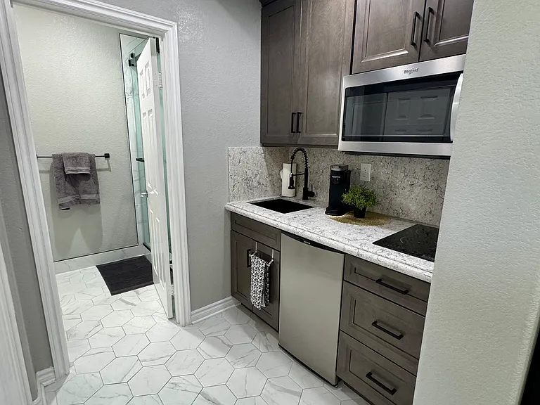 New kitchenette equipped with microwave, two burner cooktop, sink, refrigerator, Keurig coffee maker, and essentials including utensils, pans and dishes.