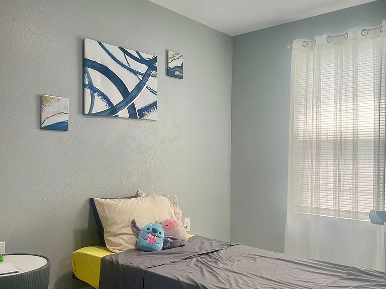Bedroom with a comfortable bed, tiled flooring, and a large window with sheer curtains for ample natural light.