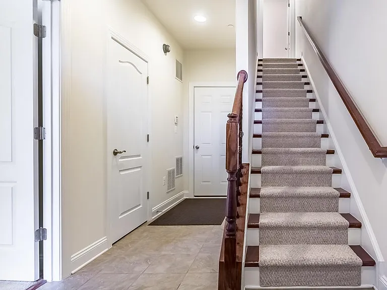 Beautiful hardwood staircase with carpet runner. The hallway and front entrance vestibule area covered by luxury ceramic tile and leads to bedroom suite and 2-car garage in the back.