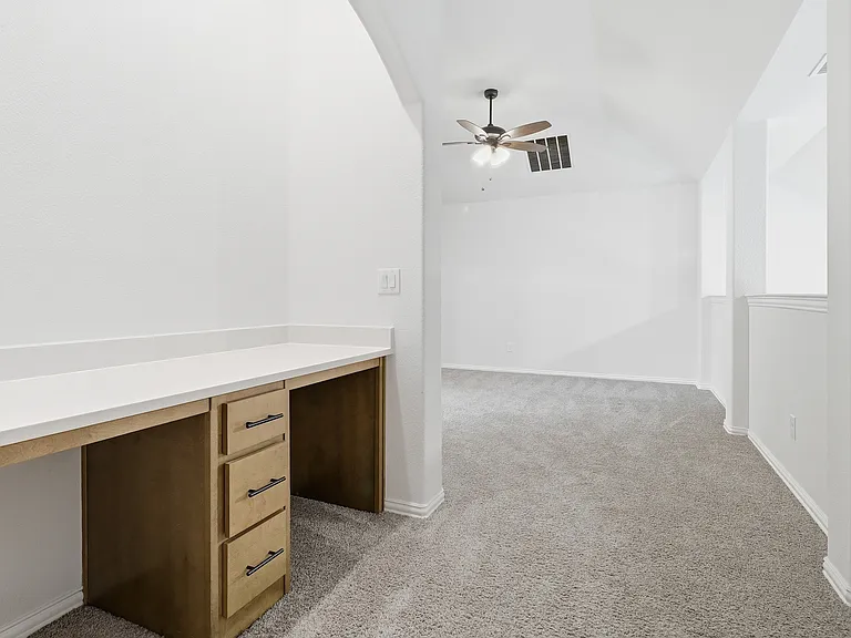 Built-in desk with a light wood-finish and white countertop, featuring three drawers with dark hardware