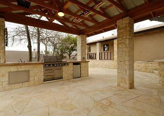 Stunning and very large covered outdoor living/kitchen entertainment area with a large grill, mini-refrigerator, and sink with hot/cold water.