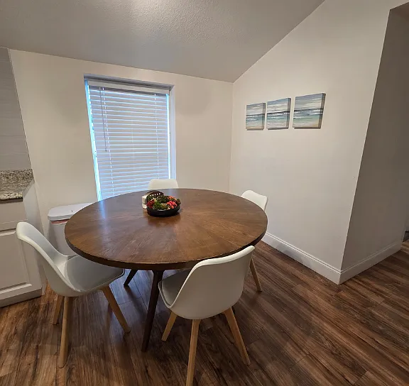 Dining area with a beautiful window, elegant blinds, wall art, and seating for four.