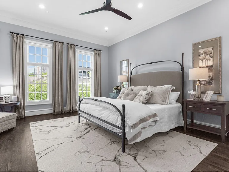 The 3rd-floor is dedicated to the primary suite with tall windows, soft gray walls, dark wood floors, an indoor fireplace, and a neutral-toned bed styled with layered pillows and textured bedding.