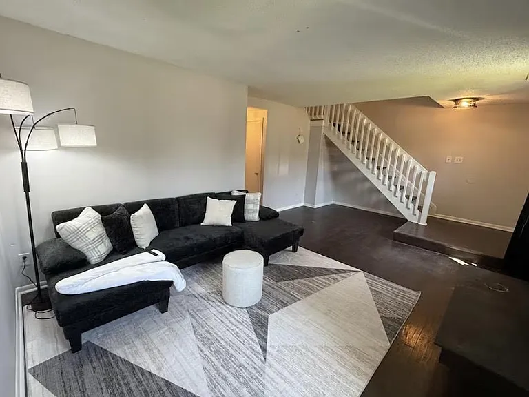 Open living area with sectional seating, accent rug, and easy flow to the staircase and adjacent rooms for shared use.