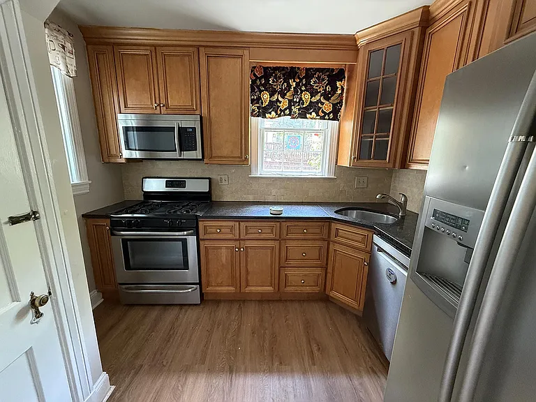 A small kitchen with fridge, oven, microwave and dishwasher. To the left is a door to the basement.