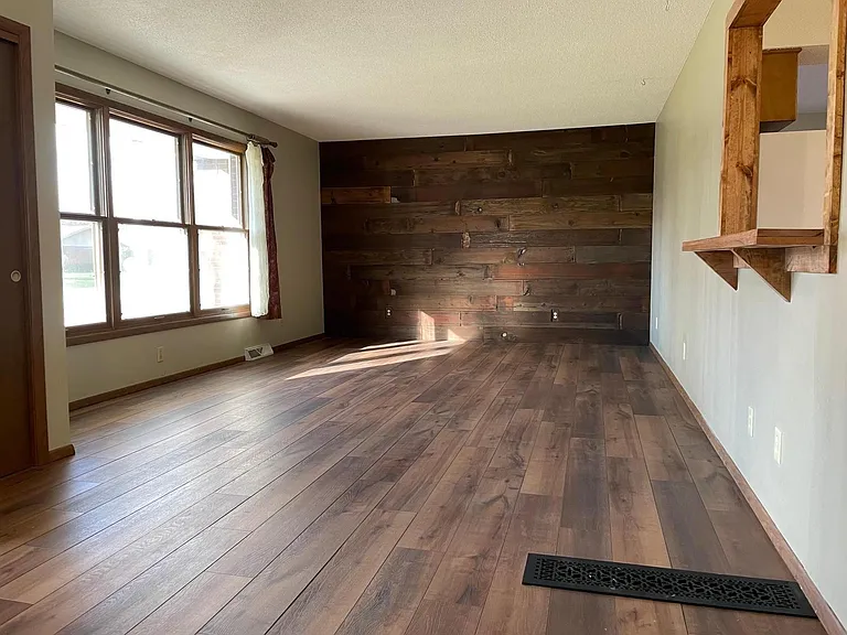 Large living room with accent wall, large widow, and passthrough bar to dining room/kitchen.