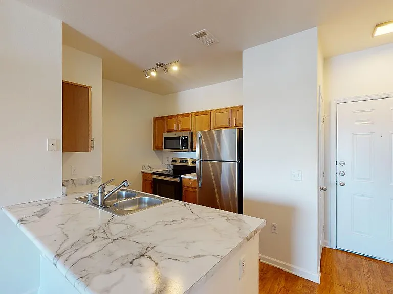 Apartment kitchen with stainless steel appliances, wood-style flooring, and marble-style countertops (shown here). Quartz-style countertops are available in select homes.