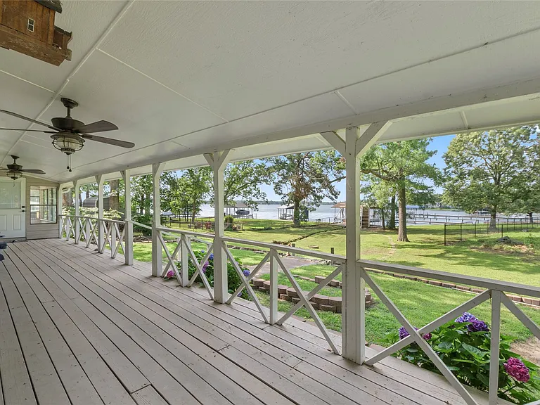 Expansive covered porch featuring wood-finish flooring, multiple ceiling fans, and decorative railing
