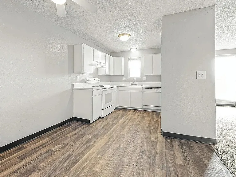 Bright open kitchen with modern white cabinetry and sleek wood flooring, leading to a sunlit living room.