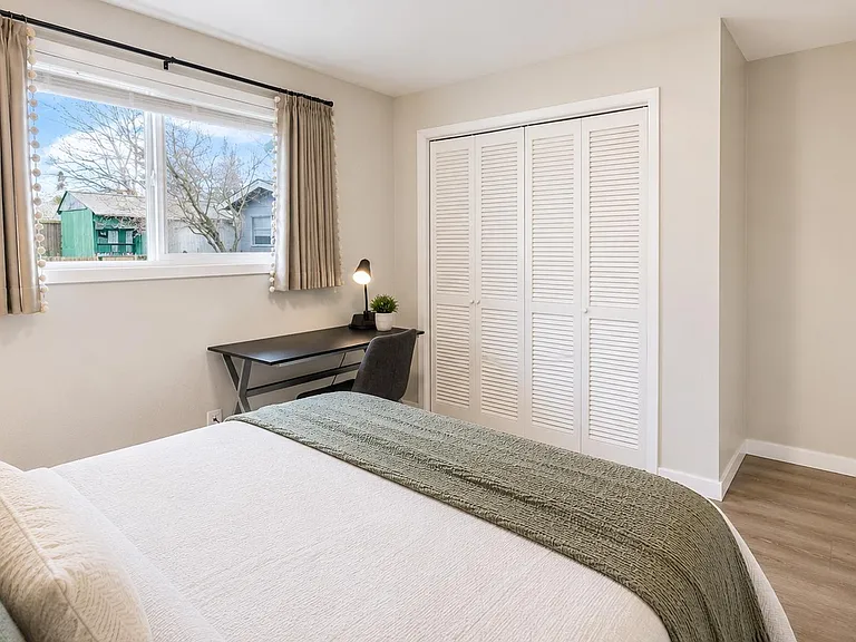 Bedroom with a large window, dedicated desk nook, and a wide closet with louvered sliding doors for storage.