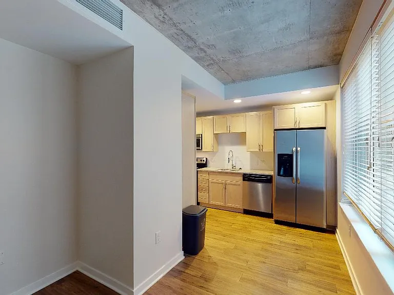 Apartment kitchen with stainless steel appliances, dining and living room with wood-style flooring.