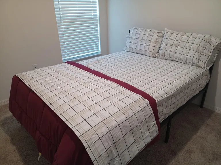 Furnished bedroom featuring a full-size bed, soft carpet, and a window with blinds for light control and privacy.