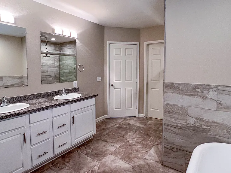 Another view of the updated primary bath, with dual sinks, granite countertops, and the walk-in closet conveniently located just next to the entry to the bathroom.