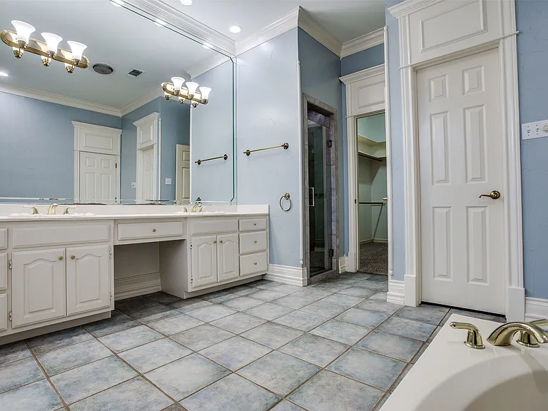 Full bathroom featuring double vanities, cabinet and drawer space galore, jetted tub, shower stall, ornamental wood molding, and tile flooring. Plus a large walk-in closet.