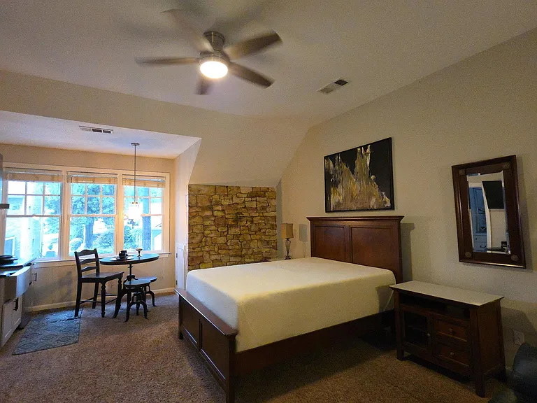 Spacious bedroom with ceiling fan, large windows, and space for a sitting or dining nook; includes bed and nightstand.
