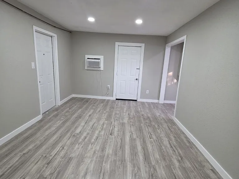Open, flexible room with wood-look flooring, recessed lighting, and multiple doorways for easy access to adjacent spaces.