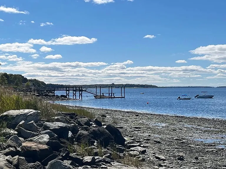 The waterfront along the bay, with views of the dock. There is a private beach to the left of the dock