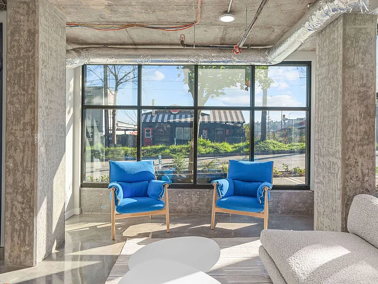 This bright living room features comfortable blue couches, large windows that allow natural light, and a spacious layout.