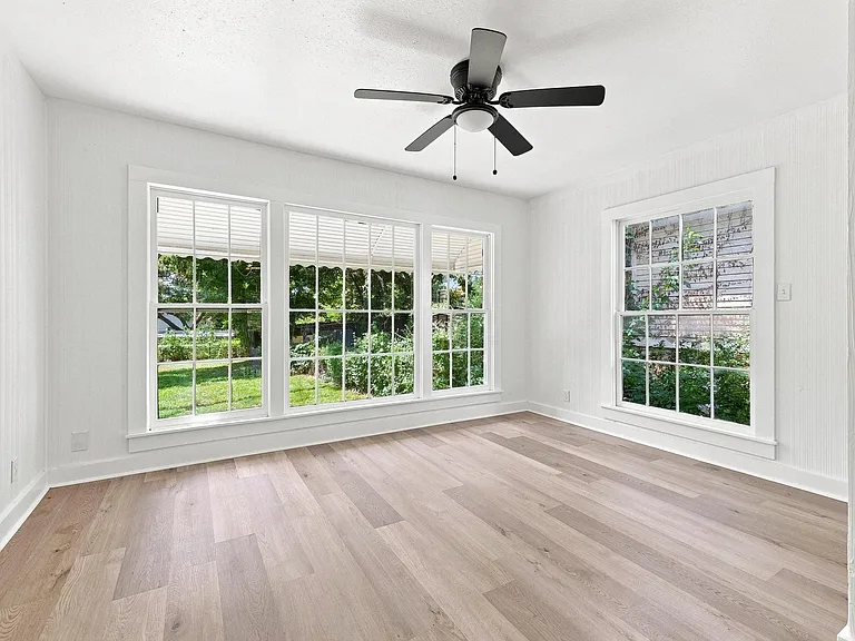 Bright interior featuring light wood-finish flooring, white paneled walls, and a black ceiling fan with an integrated light kit
