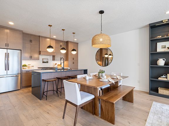 Modern kitchen and dining area with wood cabinets, stainless steel appliances, island with bar stool