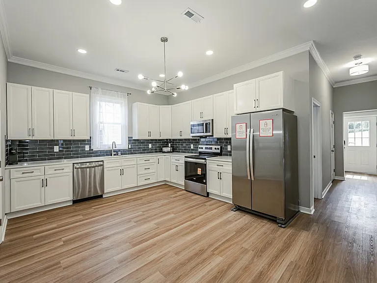 Spacious kitchen with abundant white cabinetry, stainless appliances, and a large countertop workspace with windowed sink.