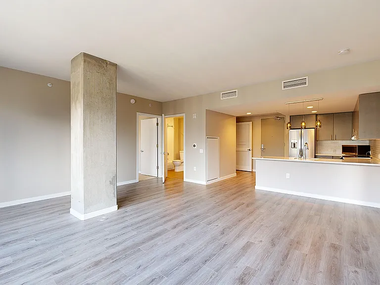 Apartment kitchen with stainless steel appliances, dining and living room with wood-style flooring.