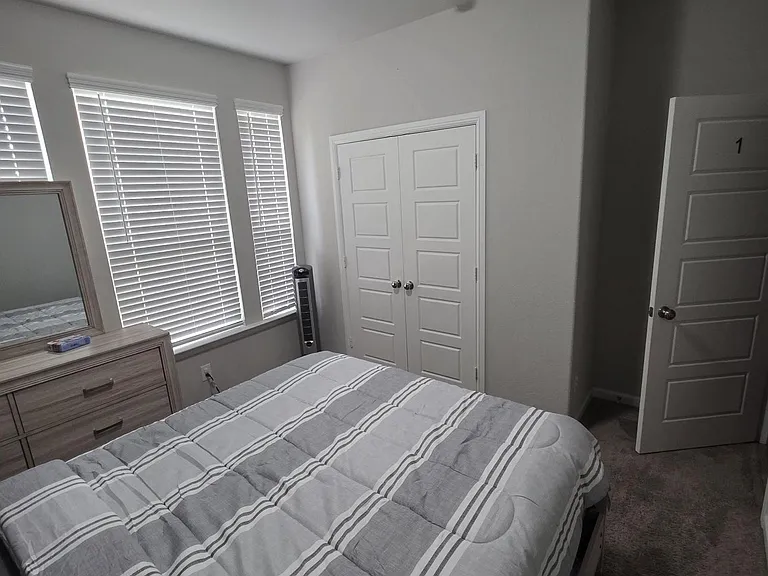 Comfortable furnished bedroom with a full bed, dresser, and closet, plus multiple windows with blinds for privacy.
