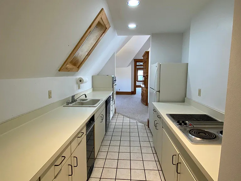Kitchen from back entry, w/dishwasher, range, grill, oven, skylight. There is open storage above the cooktop.