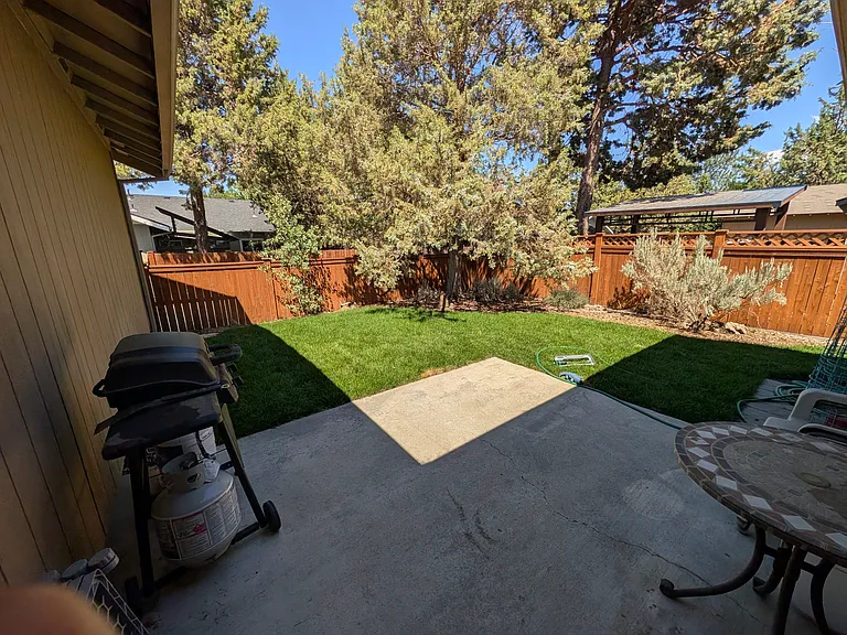 Fully enclosed back yard with large juniper tree, new sod, and xeriscaped border with large established sage. BBQ grill, table with chairs, paved patio