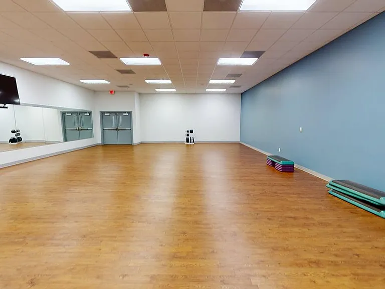 Spacious fitness studio with polished hardwood floors, mirrored wall, and vibrant blue accent wall, perfect for yoga or aerobics classes.